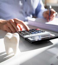 Implant dentist in Blaine using a calculator next to a model tooth.