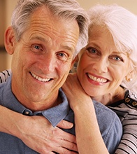 Older couple with dental implants in Blaine smiling and hugging
