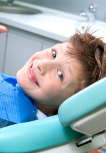 child giving thumbs up while sitting in dental chair 