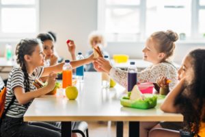 four girls eating school lunches at cafeteria table 